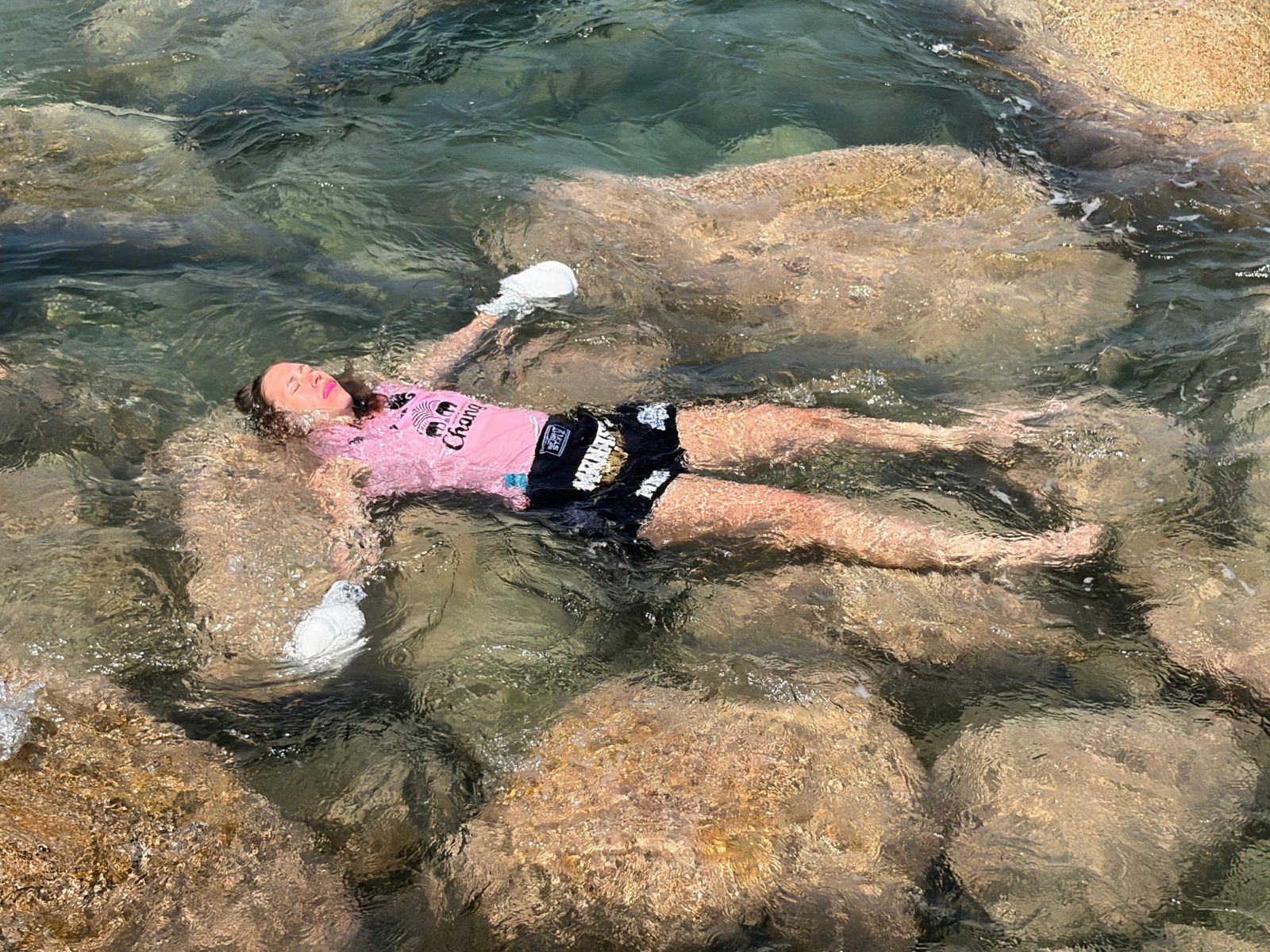 Merel Severs drijft op de rug in helder water, in bokshandschoenen en Muay Thai-short